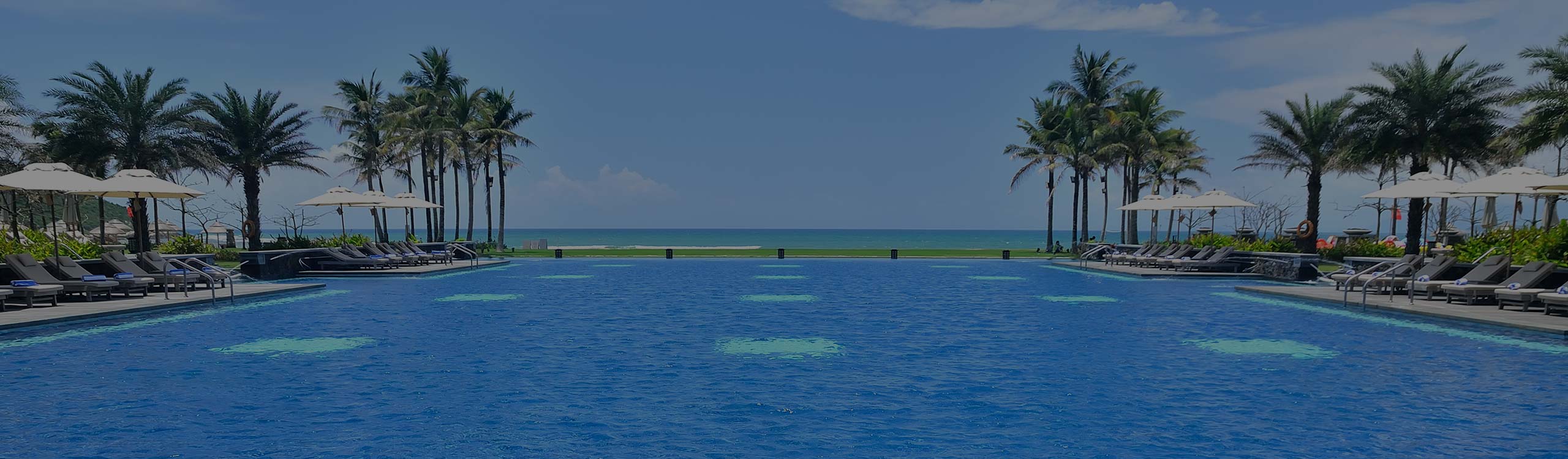 Older man with gray hair sitting in lounge chair by pool with arms behind head relaxing